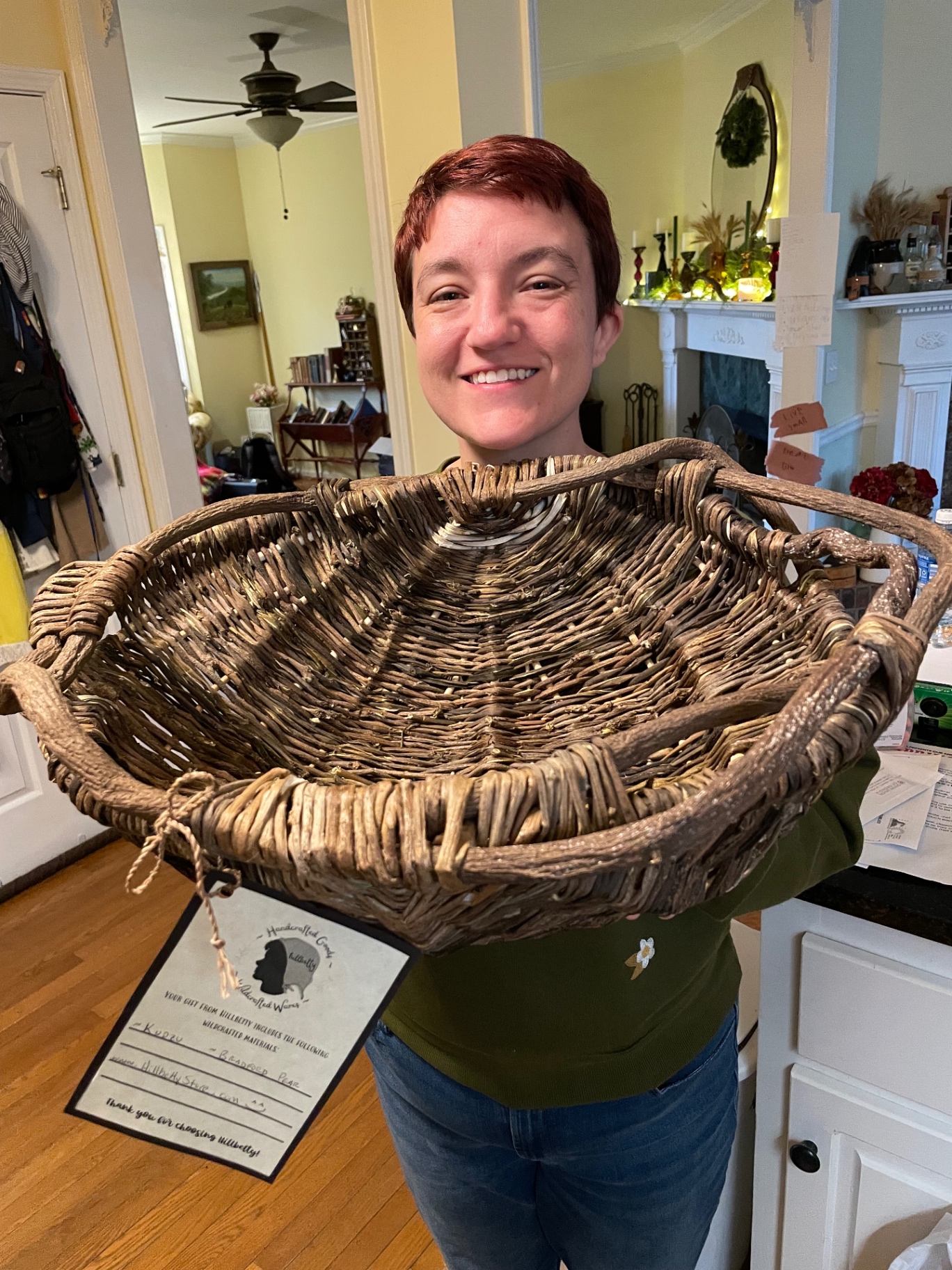 Hannah holding a large basket she wove from kudzu and Bradford pear, with a HillBetty tag tied on